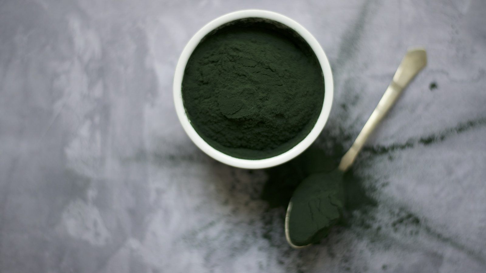 Poudre vert foncé de chlorella dans un bol en céramique, à côté de quelques gélules vertes