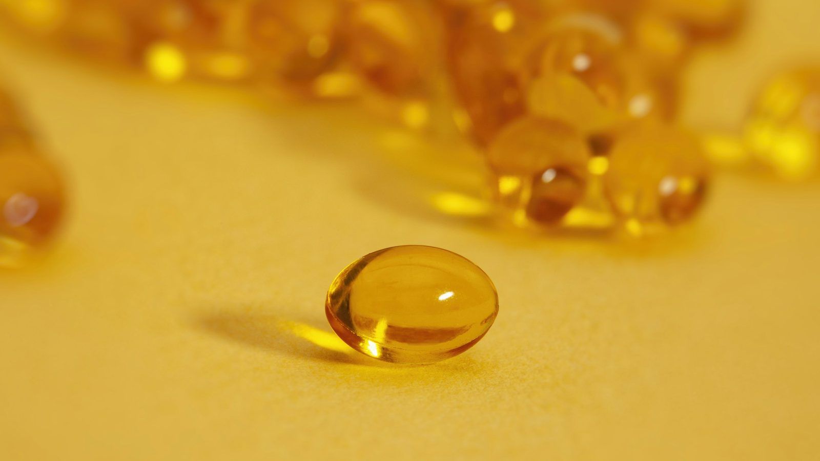 Capsules molles orangées de coenzyme Q10 posées dans une coupelle en verre, en lumière naturelle
