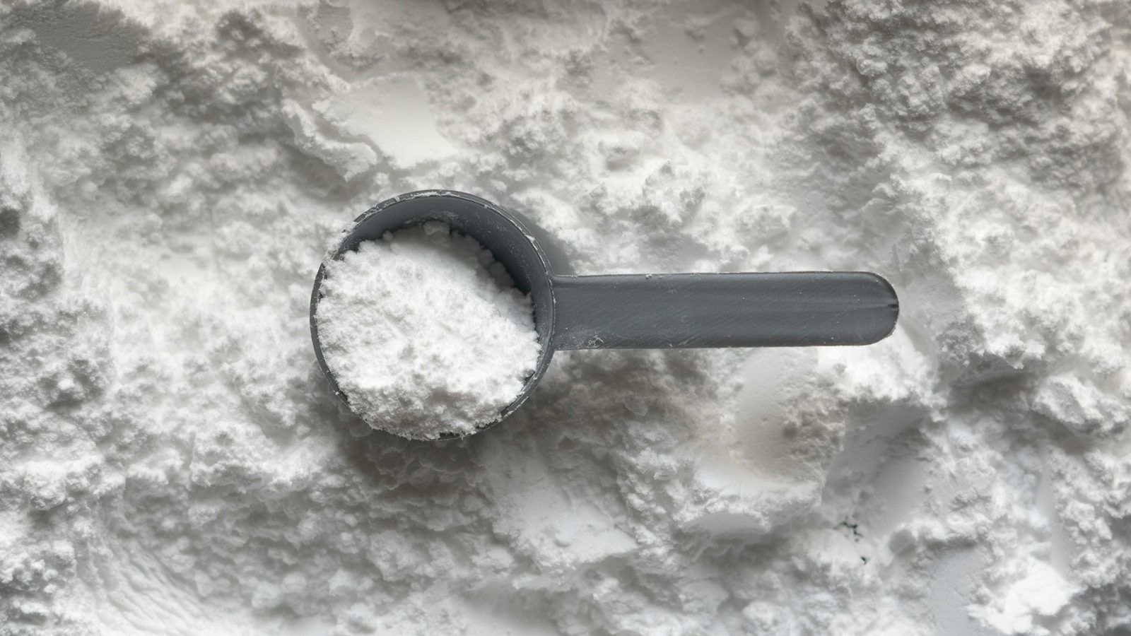 Poudre blanche de collagène marin dans une cuillère en bois, à côté d'un verre d'eau