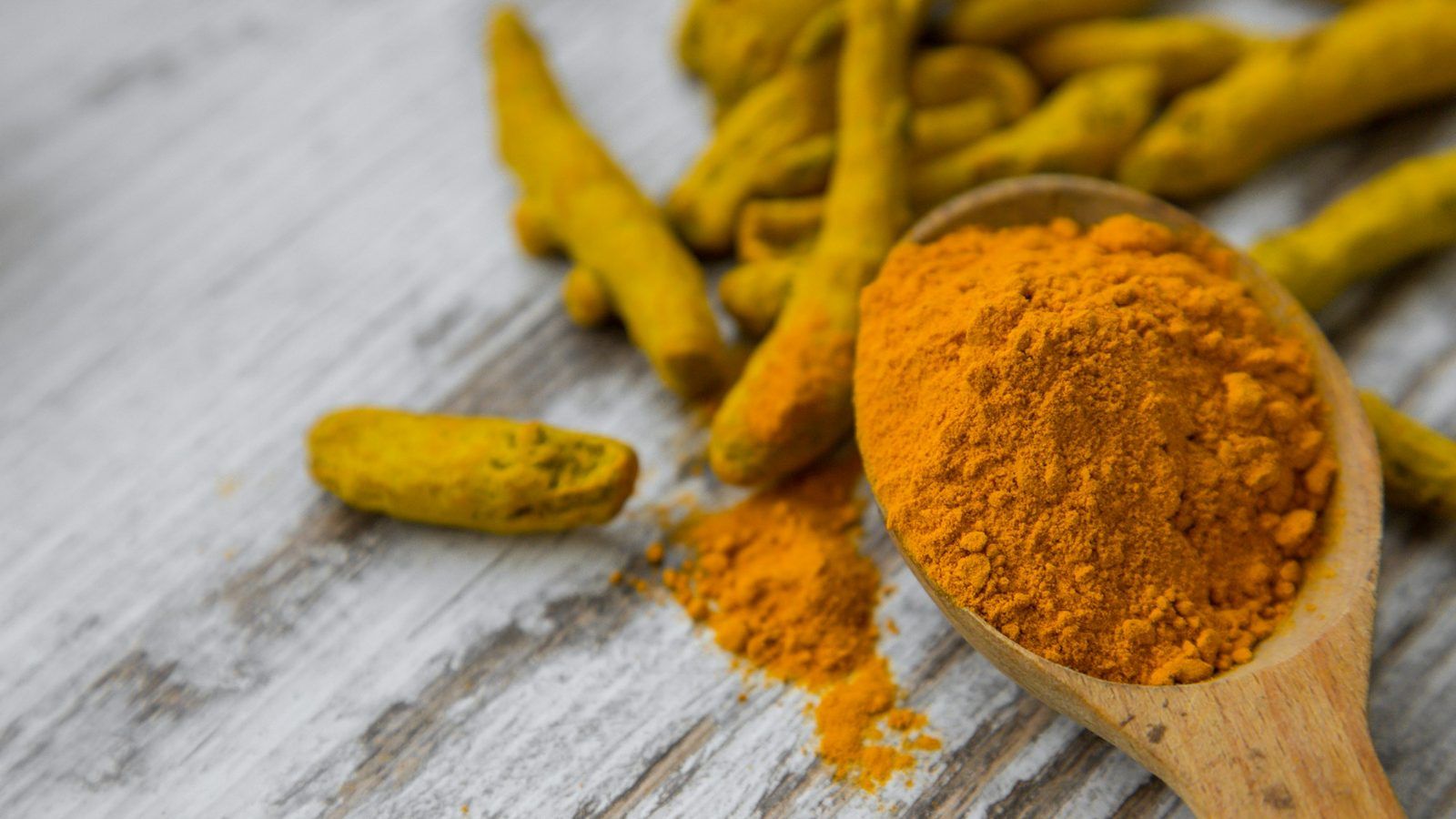Racines de curcuma fraîches coupées et poudre orange de curcuma dans un bol, à côté de gélules