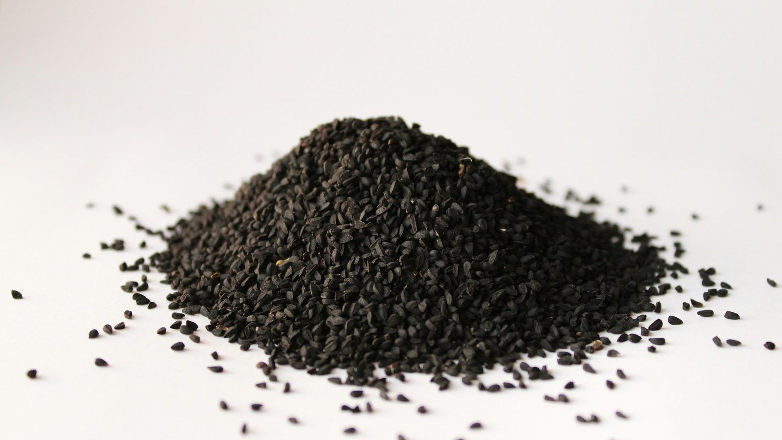 Graines noires de nigelle et petite coupelle d'huile ambrée sur une planche en bois