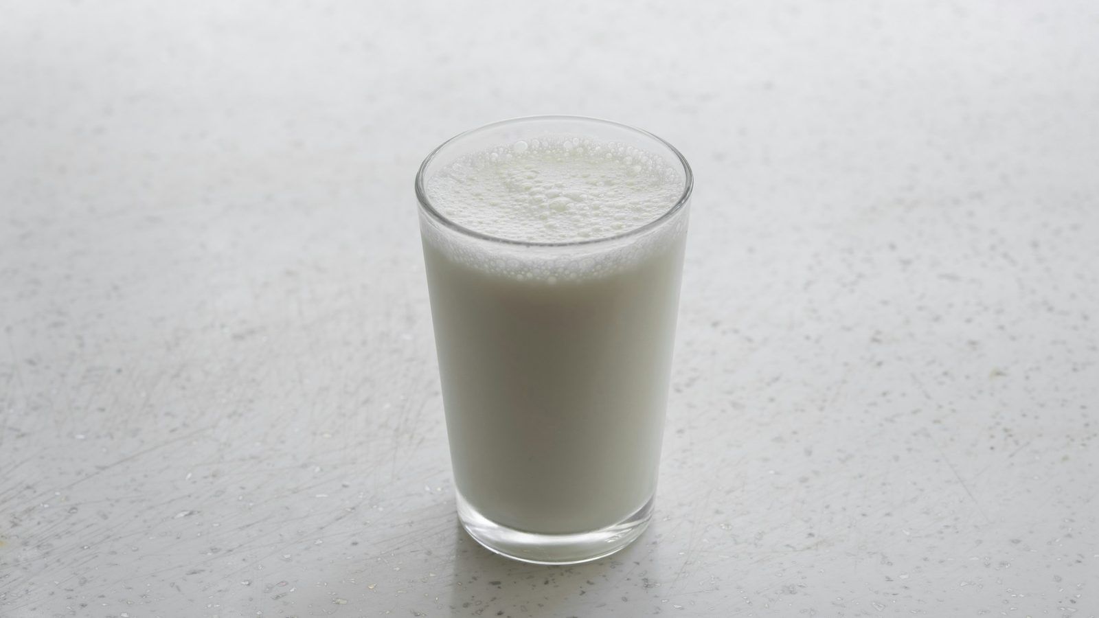 Verre de lait et gélules blanches de lactase posés sur une table de cuisine en bois