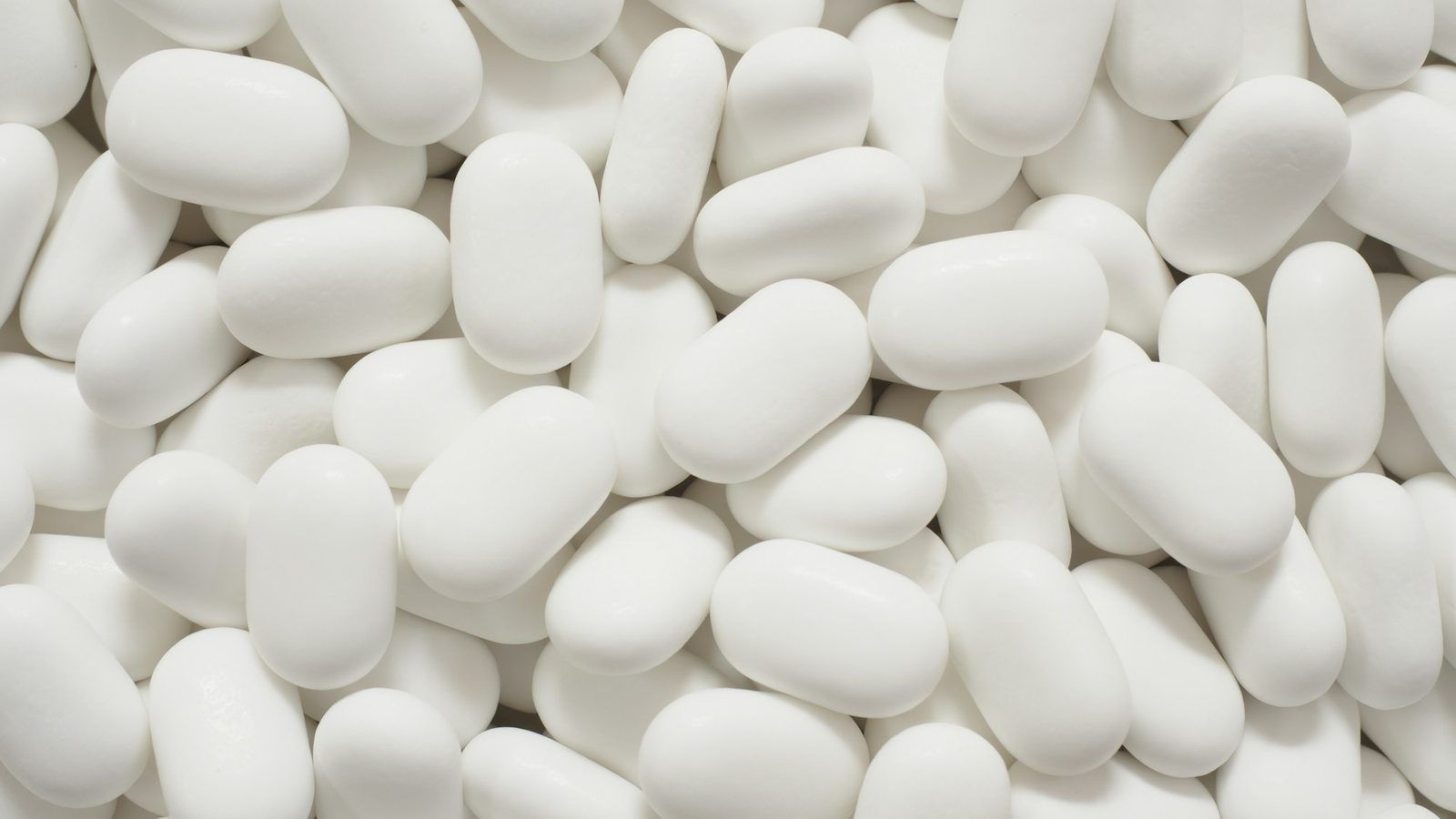 Gélules blanches de magnésium dans une coupelle en céramique, à côté d'une poignée d'amandes