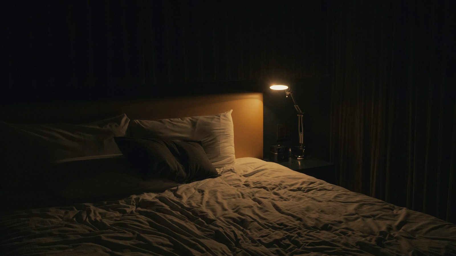 Gélules blanches posées sur une table de nuit en bois, à côté d'une lampe à la lumière tamisée