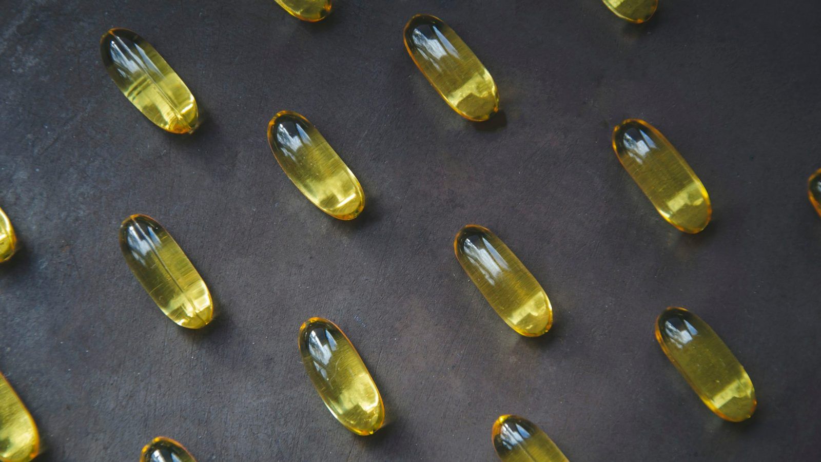 Capsules dorées d'huile de poisson oméga 3 dans une coupelle en verre, à côté d'un filet de sardines
