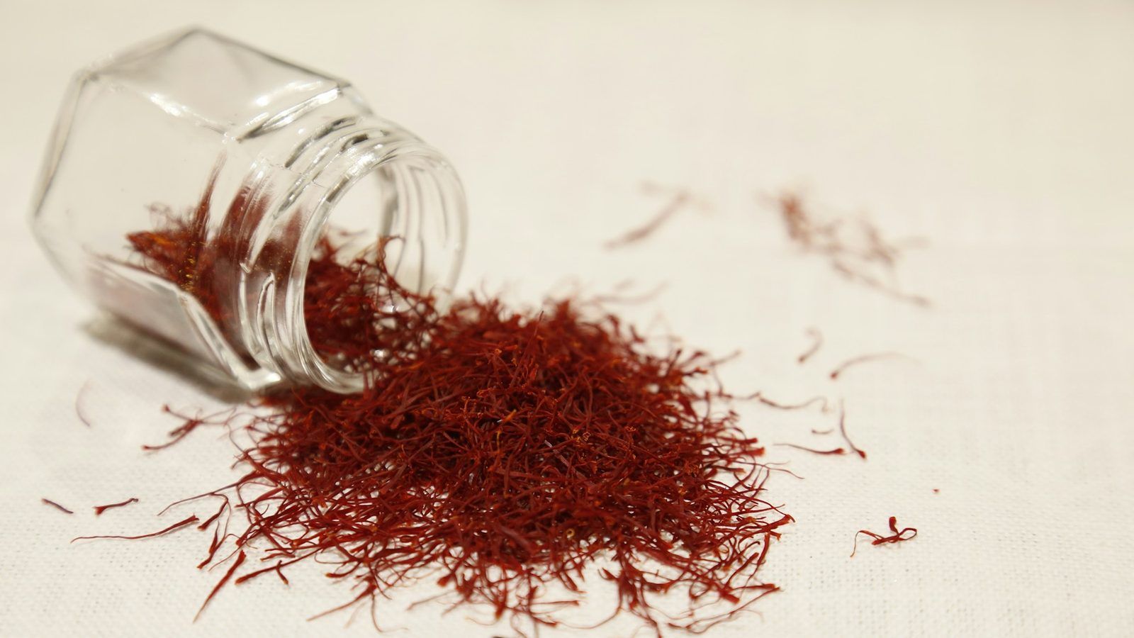 Filaments de safran rouge orangé dans une petite coupelle en céramique blanche, à côté de fleurs de crocus violettes