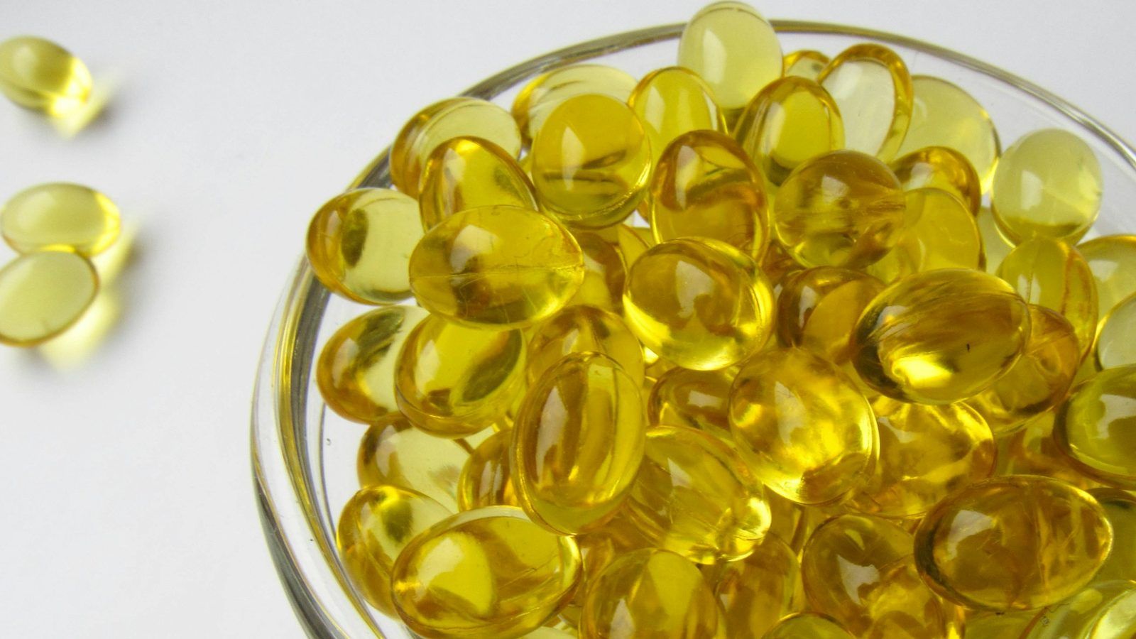 Petites capsules jaunes de vitamine D3 posées sur une table en bois éclairée par un rayon de soleil