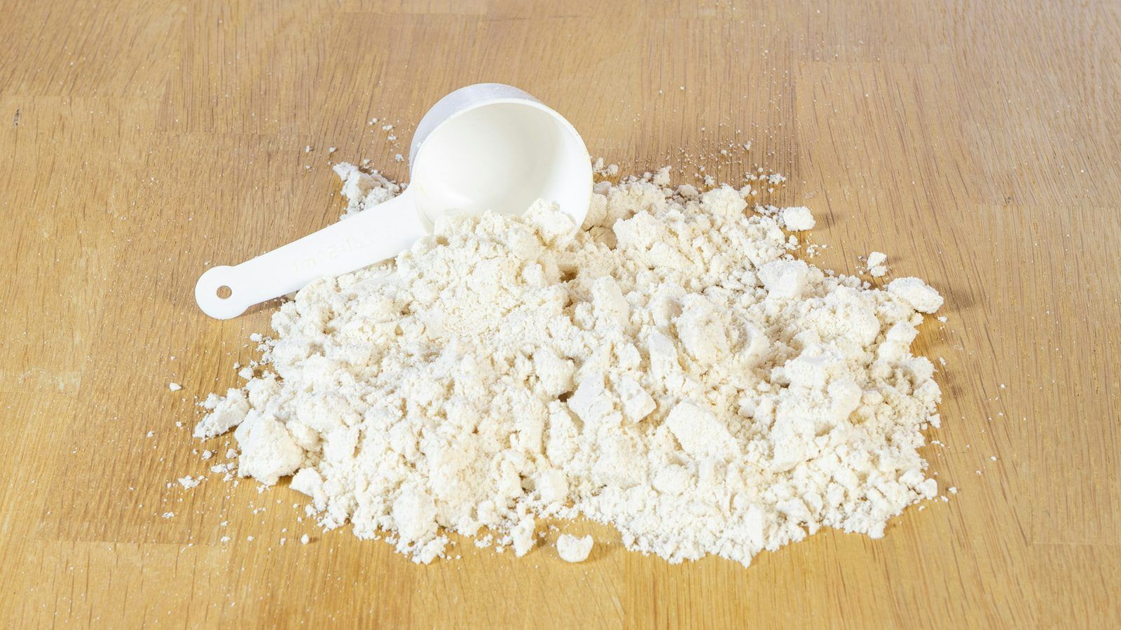 Cuillère doseuse remplie de poudre de whey protéine posée à côté d'un shaker et d'un verre de lait